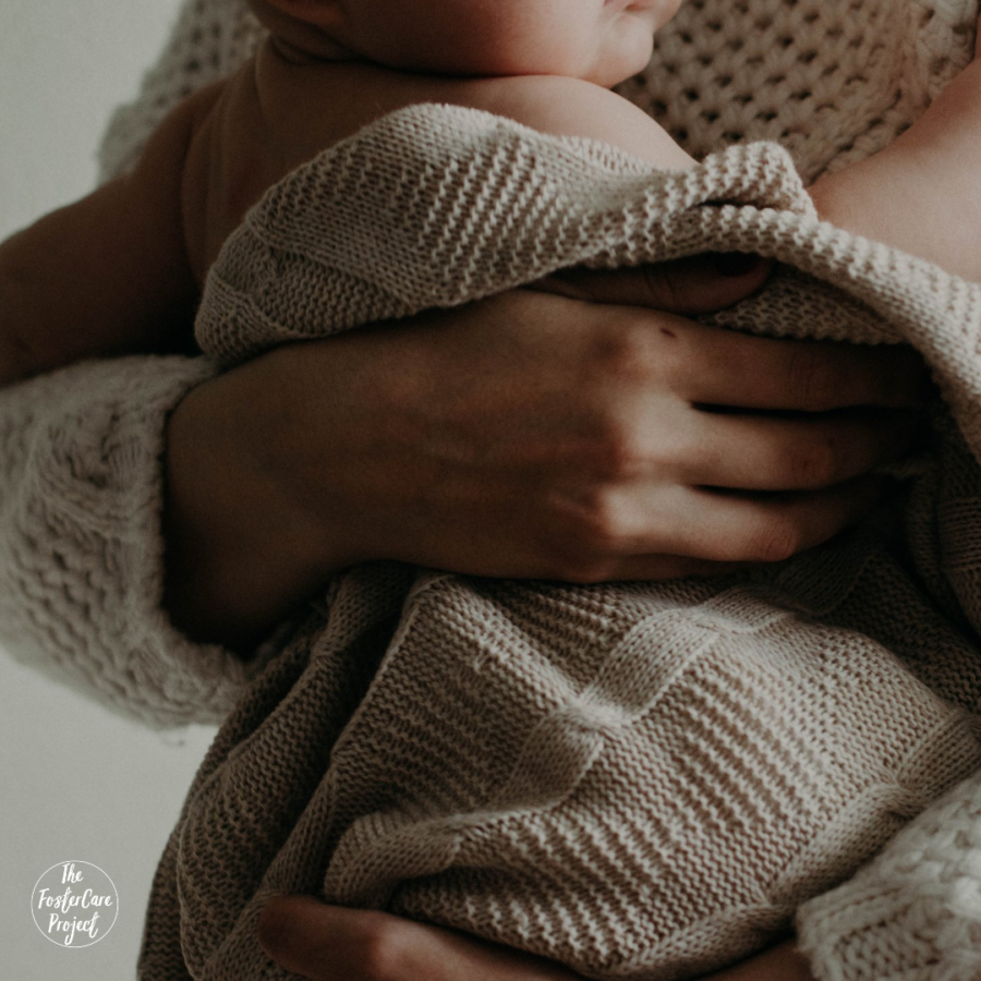 baby wrapped in a beige swaddle being held by his mother