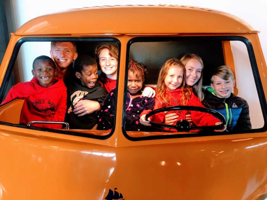 Eight kids pile into a fake bus together and smile for a photo
