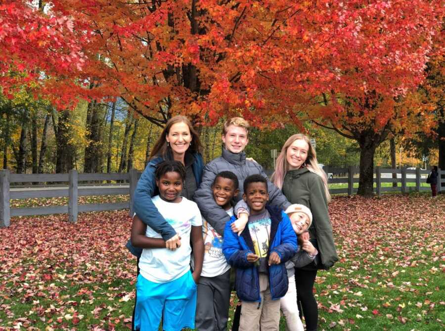 Mom takes a photo with her three adopted children and three of her five biological children with fall foliage in the background