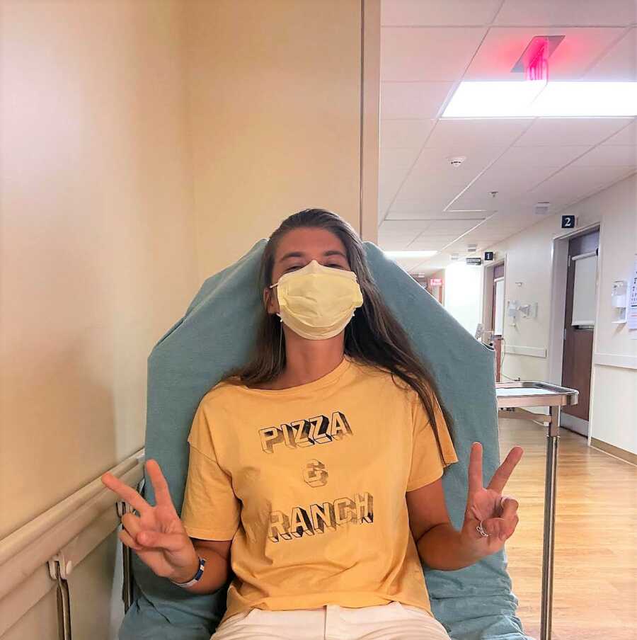 Young woman with MALS takes a photo before surgery while wearing a yellow shirt that says 'Pizza & Ranch'