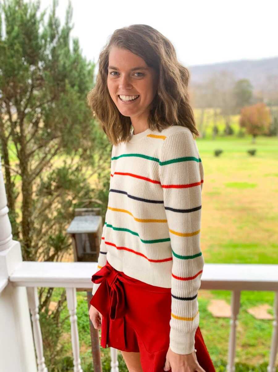Woman with chronic pain smiles for a photo in a striped sweater and red shorts