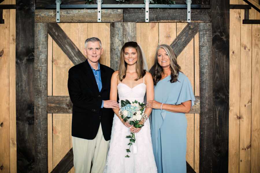 Young woman takes a photo with her parents on her wedding day