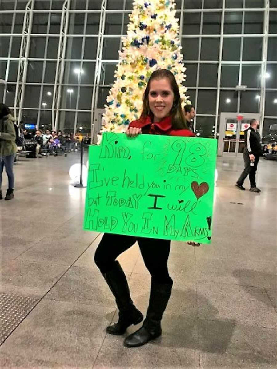 American girl waits in the airport for Dutch boyfriend holding a sign 