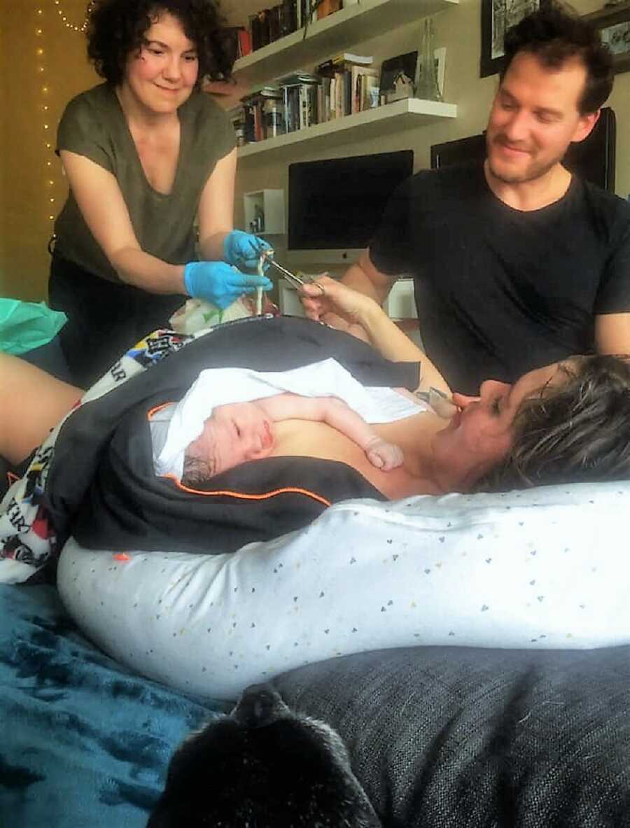 postpartum mom cuts the umbilical cord while holding newborn child 