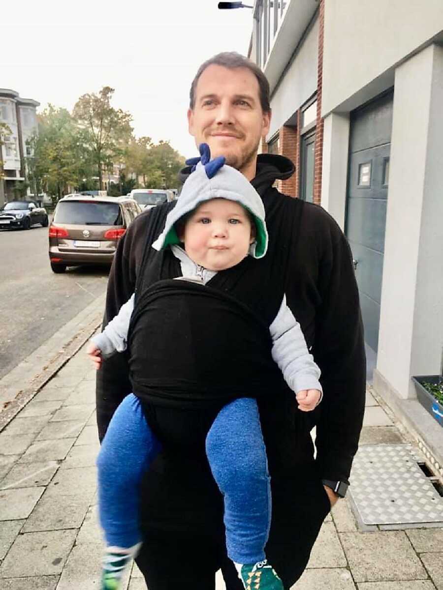 dad holding son with black baby carrier wrap on the street 