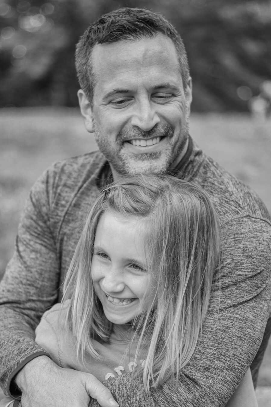 single father wraps his arms around his daughter, both are smiling and laughing