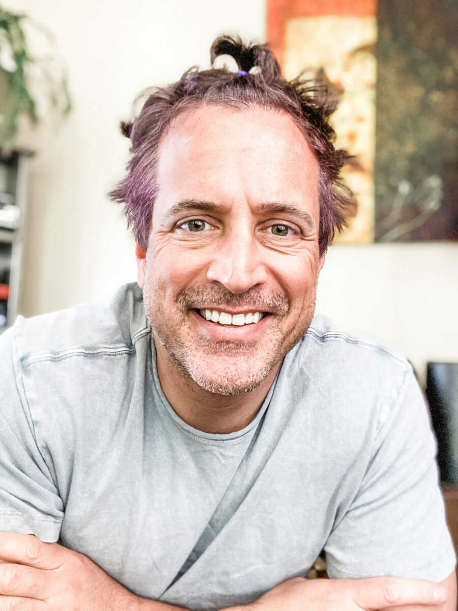 single dad smiles at camera with dyed hair and multiple small ponytails