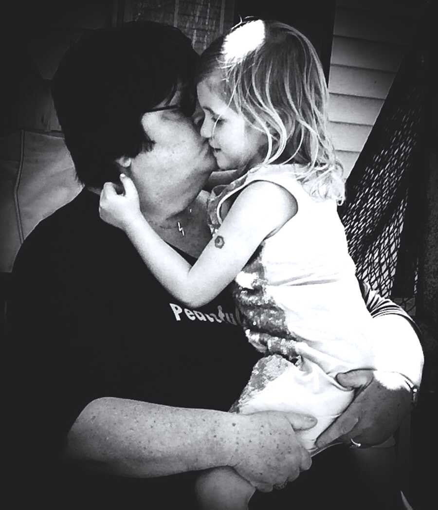 grandmother holding her granddaughter close and giving her a kiss on the cheek