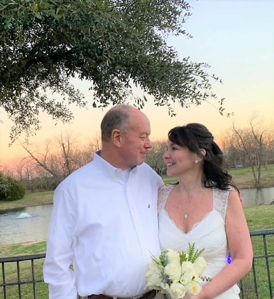 Husband and wife on their wedding day staring at each other looking in love, while bride holds a white rose bouquet with the sunset in the back