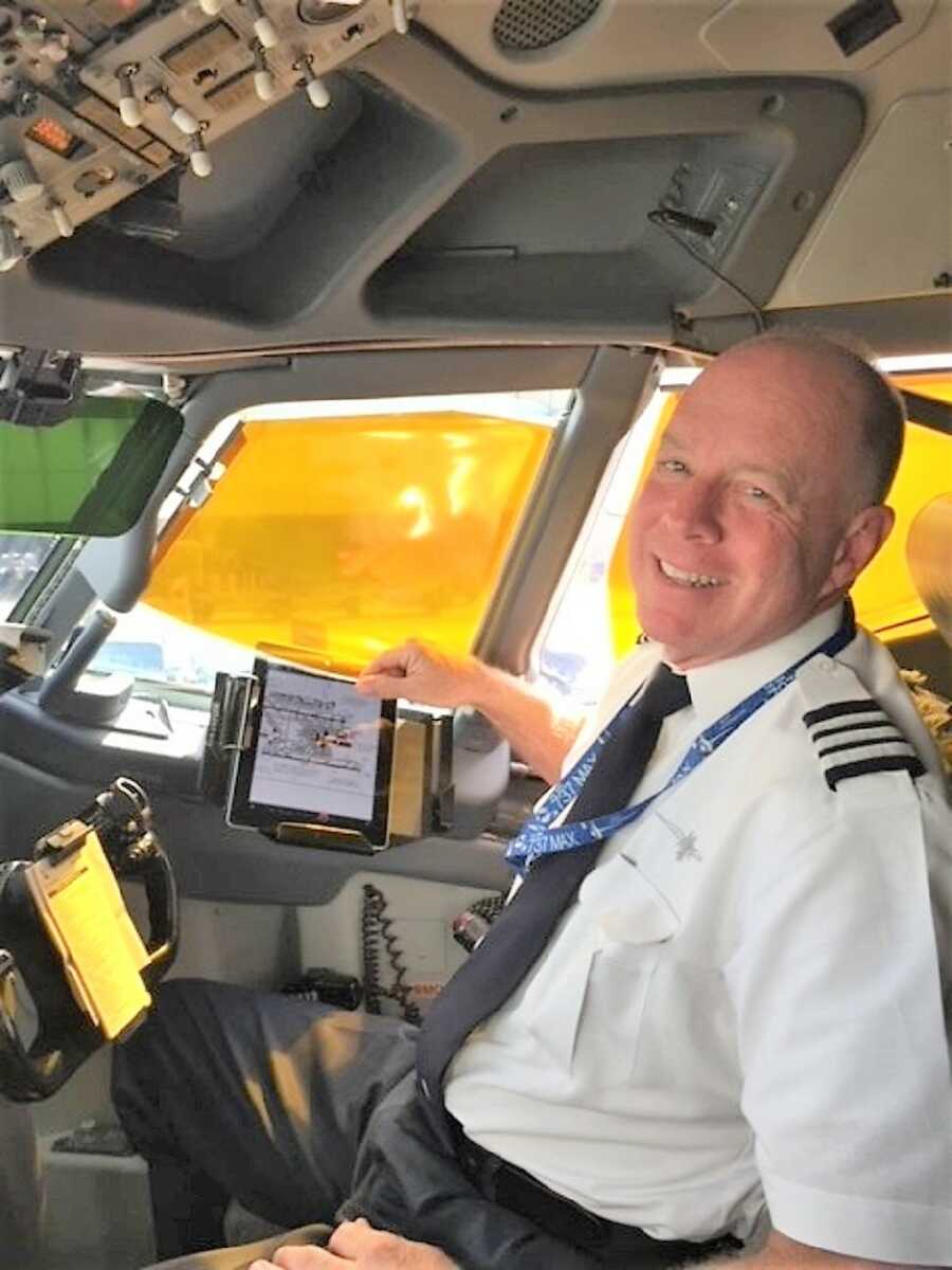 Pilot sit in the control room of an airplane while smiling at the camera 