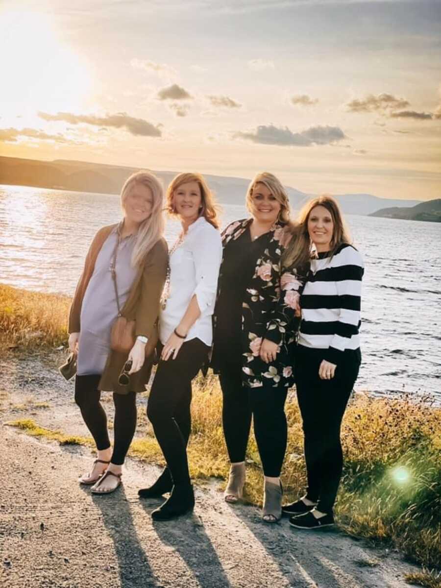 group of woman standing by the water to take a picture at sunset
