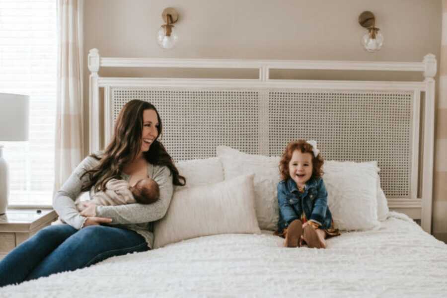 mom smiling at her daughter while breastfeeding her other child