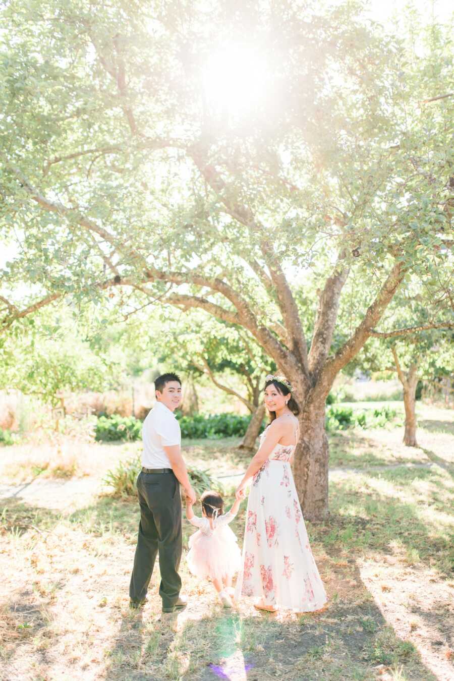 parents holding daughters hand in front of a tree