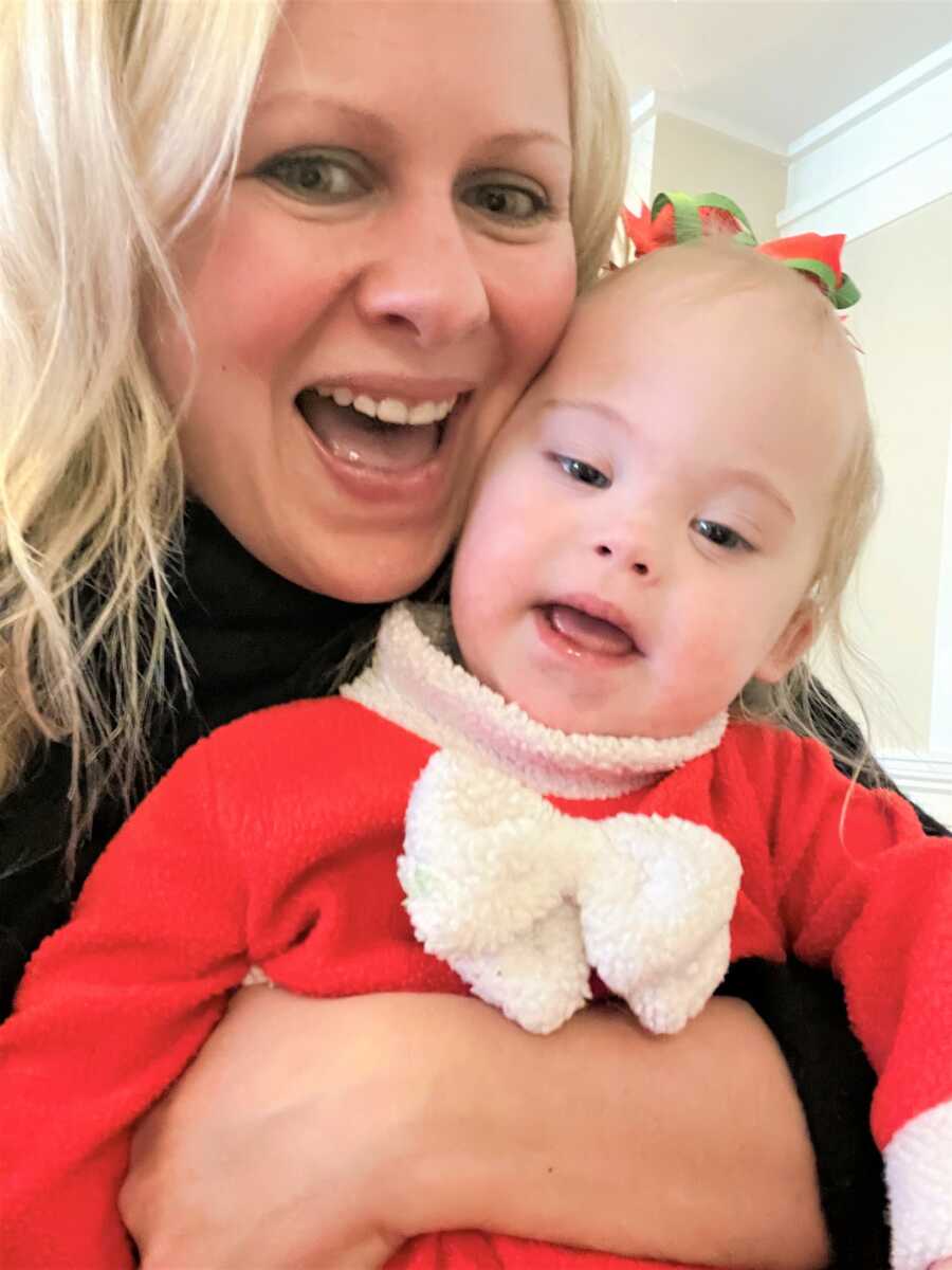 Special needs mom hugging down syndrome daughter wearing red Christmas outfit and smiling