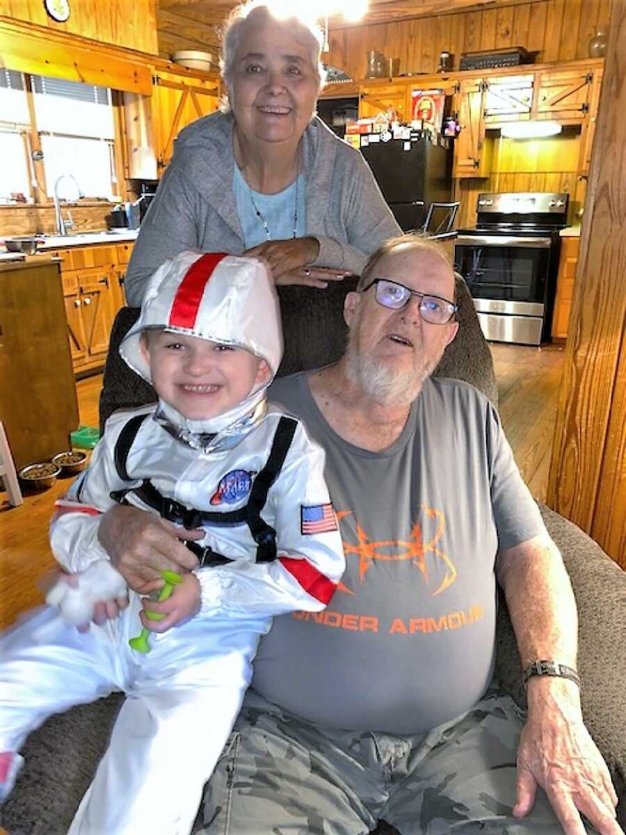 autistic boy wearing an astronaut costume sitting on his grandpa's lap with grandma in the back 