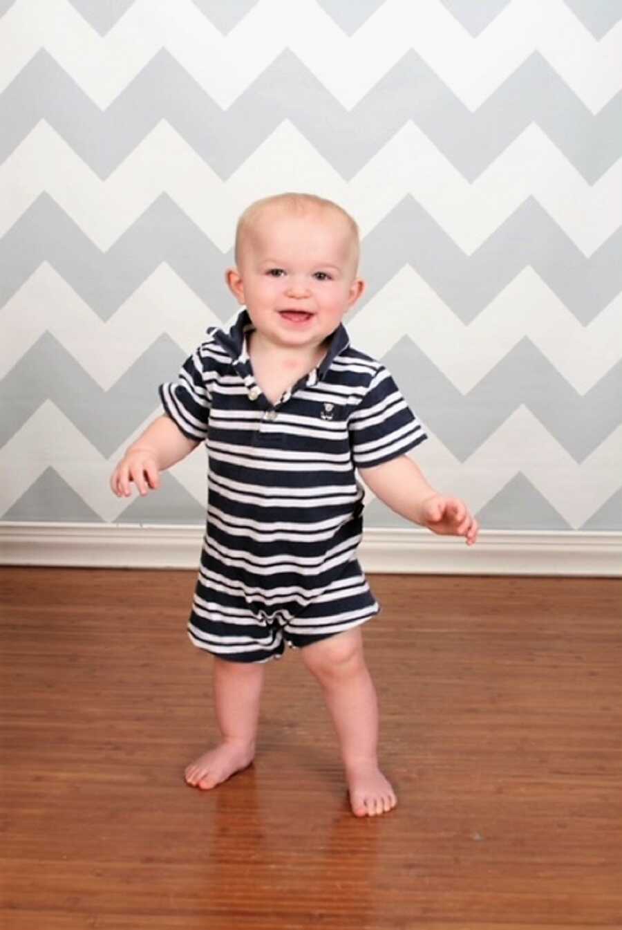 toddler with autism standing on wood floors wearing a black and white tripped shirt