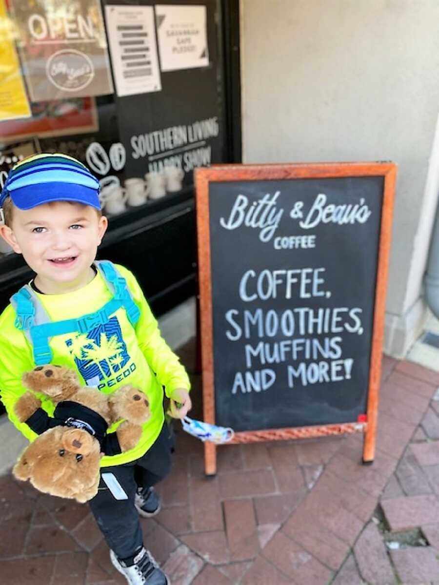 autistic boy wearing a hat and a green speedo shirt outside of a coffee place holding a teddy bear 