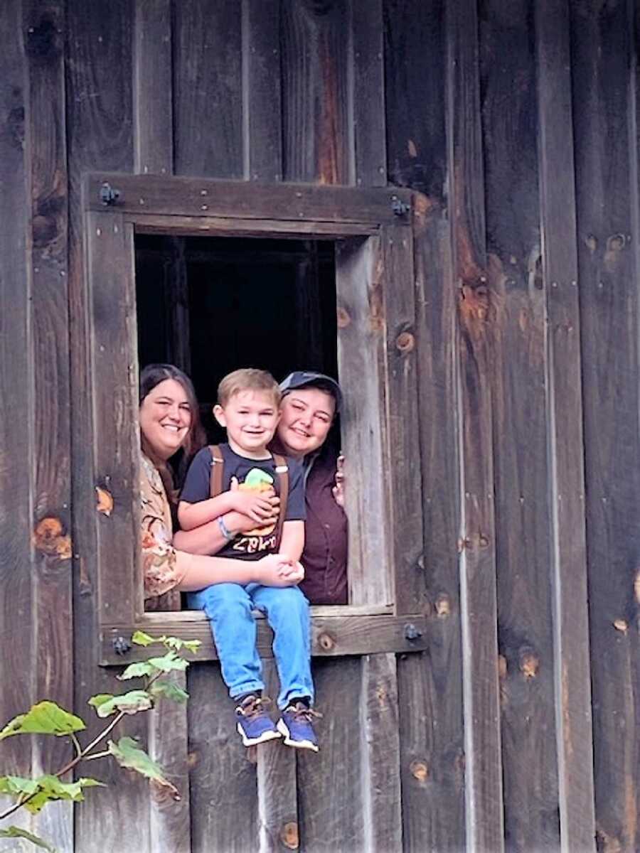 lesbian couple with their autistic son sitting on the window of a barn 