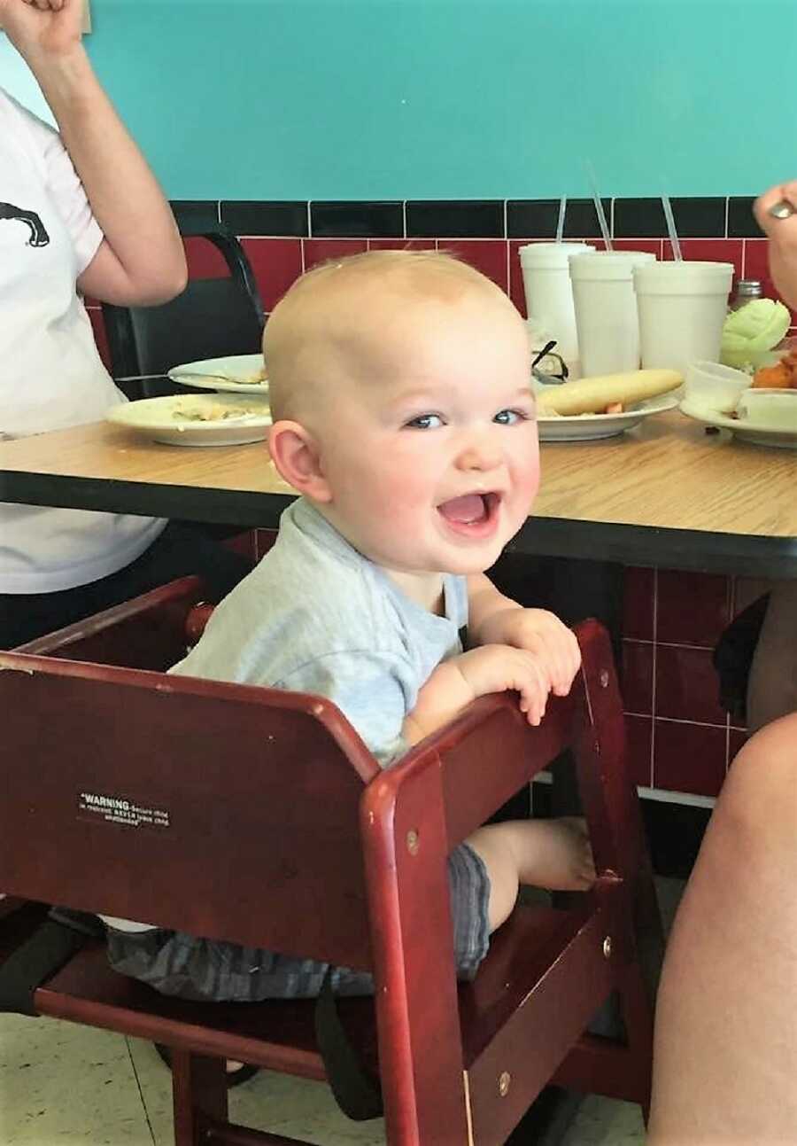 autistic baby sitting on a baby chair at a restaurant looking back and smiling