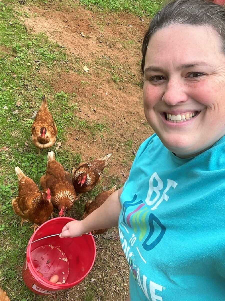 special needs home feeding her chickens carrying a red bucket 