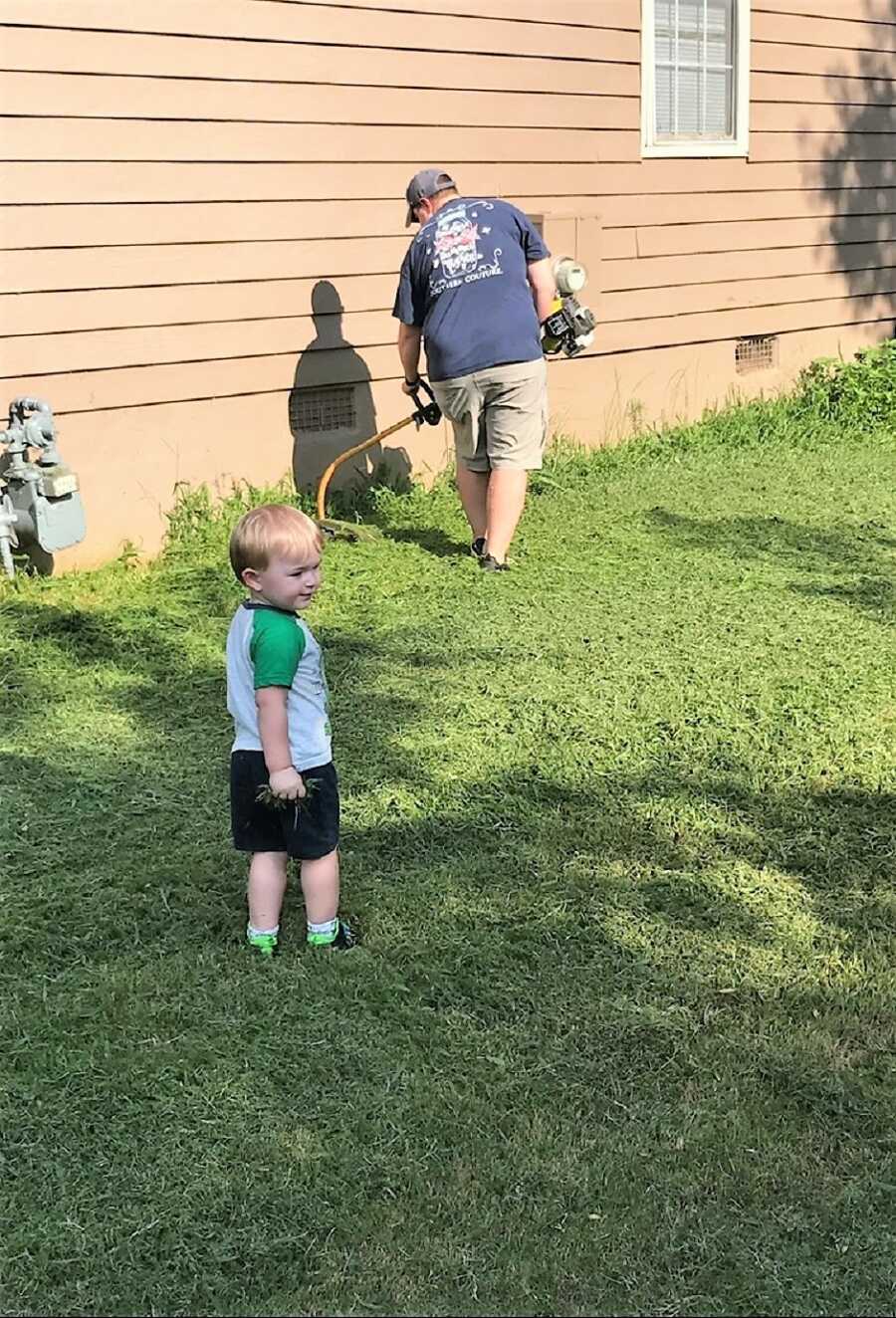 autistic boy playing in the backyard while grandparent mows the lawn 