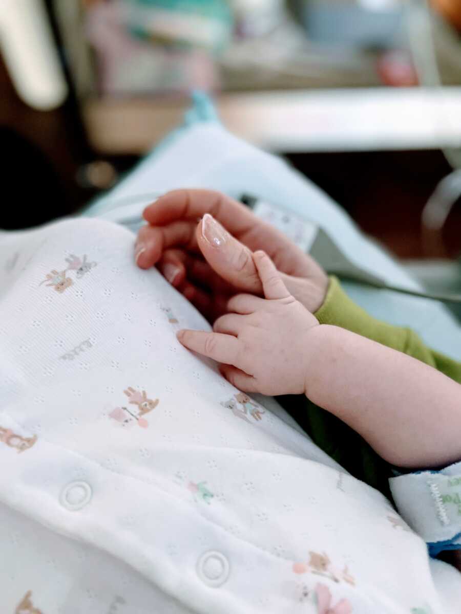 Mom holds newborn daughter's finger in her hand