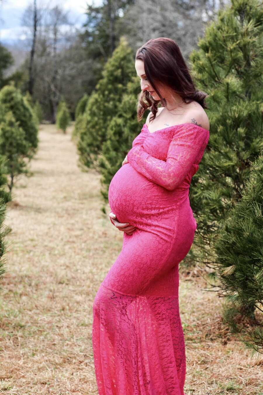 mom in a bright pink dress cradling her baby bump
