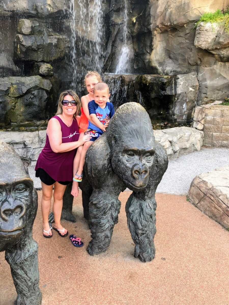 Mom takes a photo with her two kids and a gorilla statue at the zoo