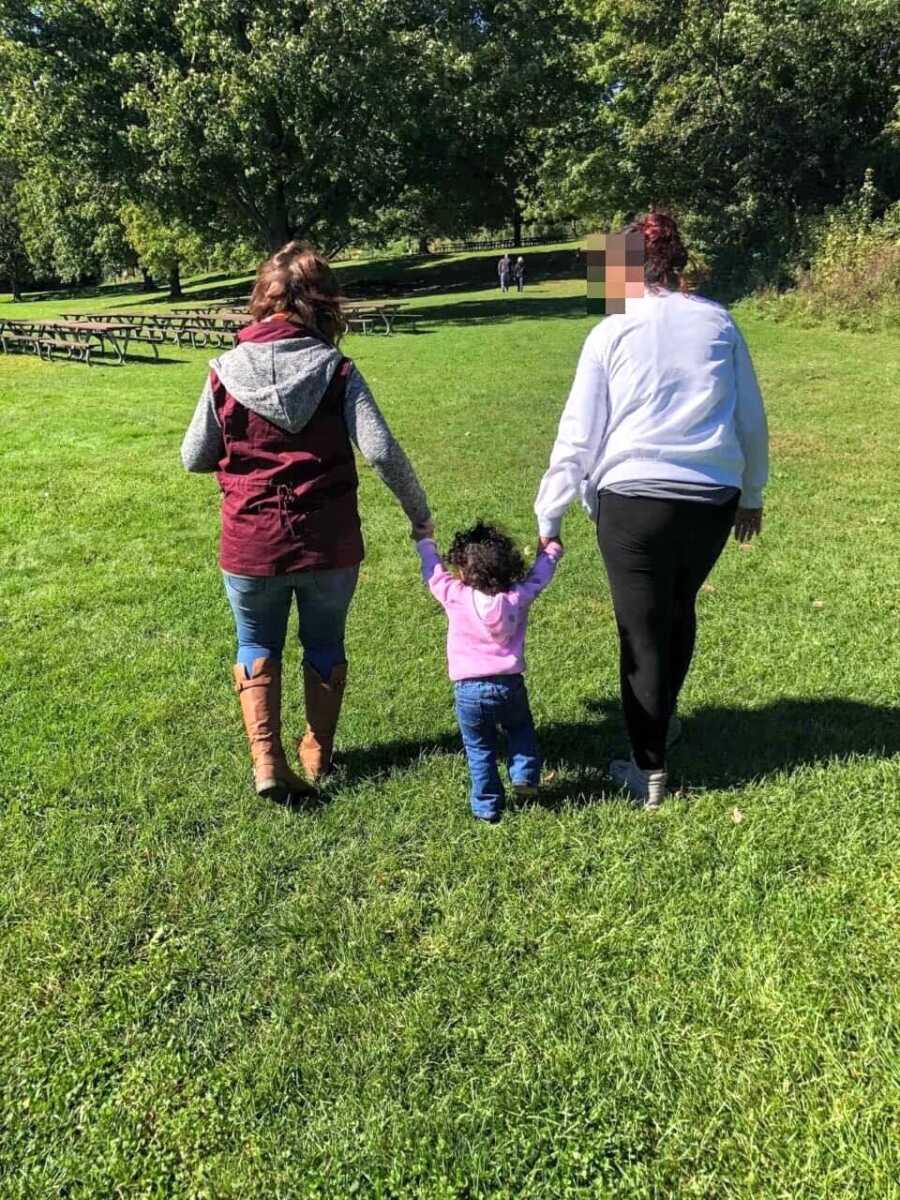 Adopted mom and birth mom walk hand in hand with daughter