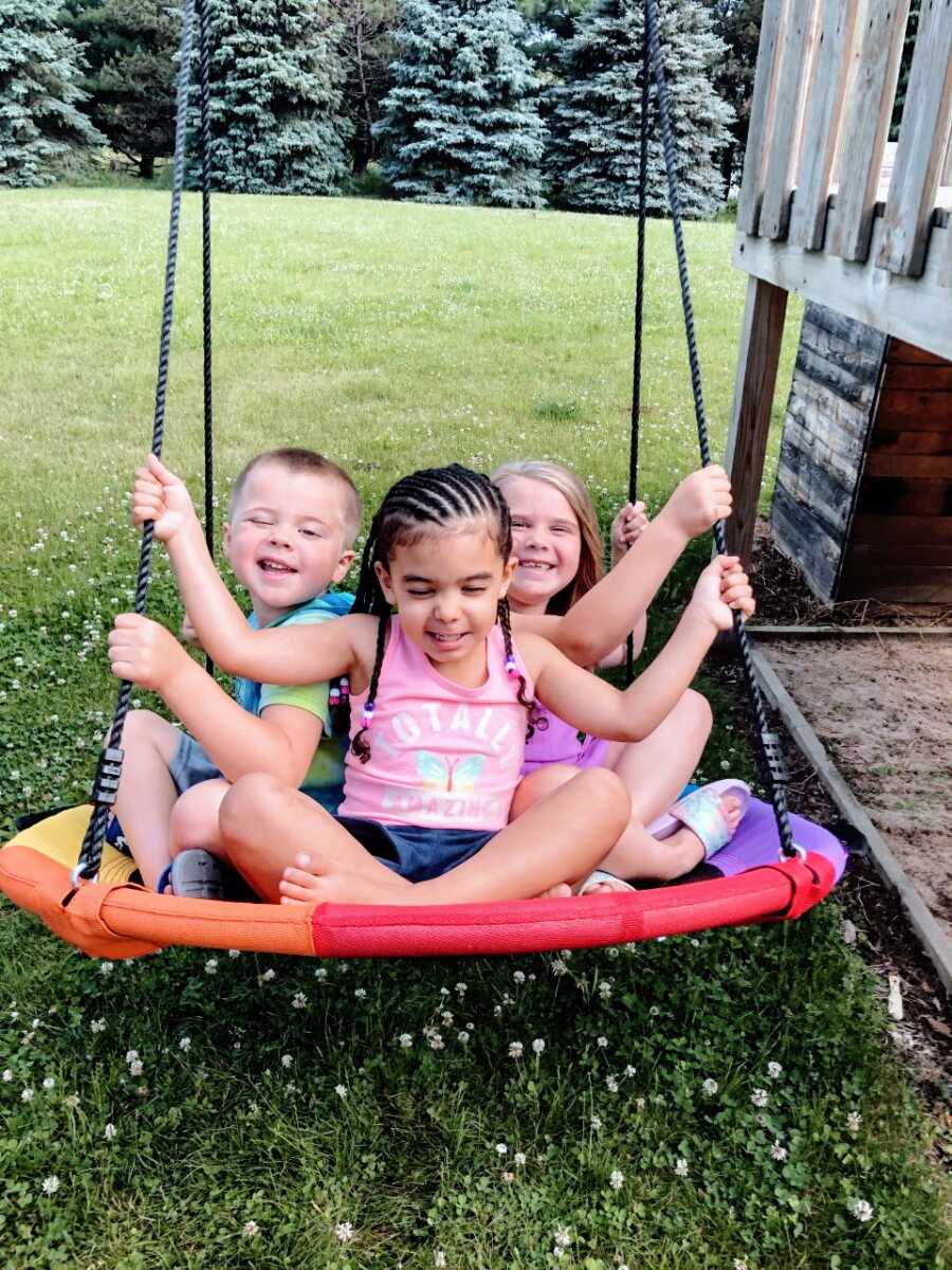 Three siblings swing together in their backyard and smile