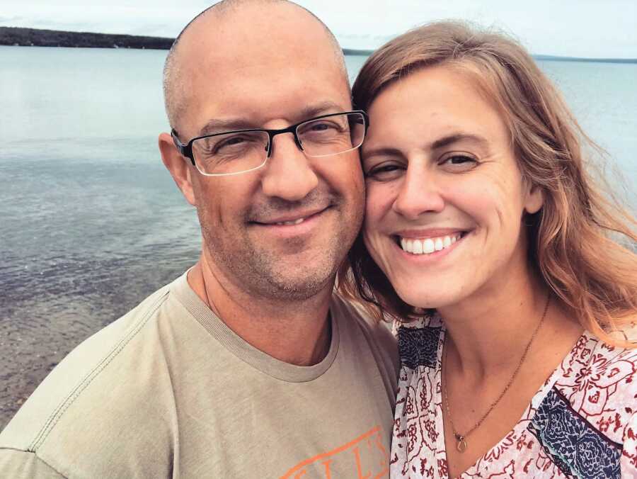 couple smiling hanging out in a lake, husband wearing glasses and gray shirt 