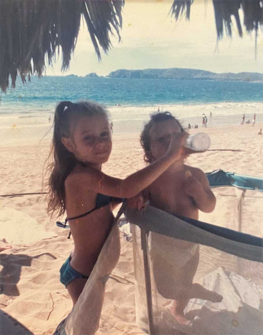 young kid bottle-feeding younger sibling in a crib at the beach 