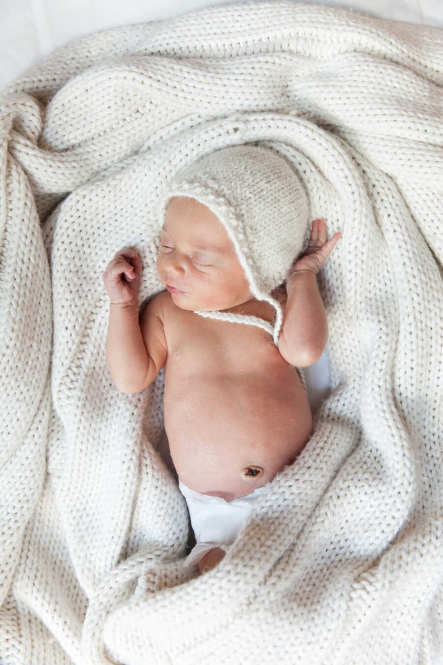 newborn baby sleeping on a white knitted blanket wearing a matching knitted hat