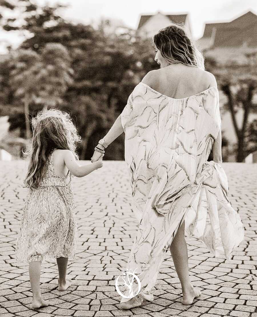 mother holding daughter's hand while walking barefooted and wearing long print dresses 