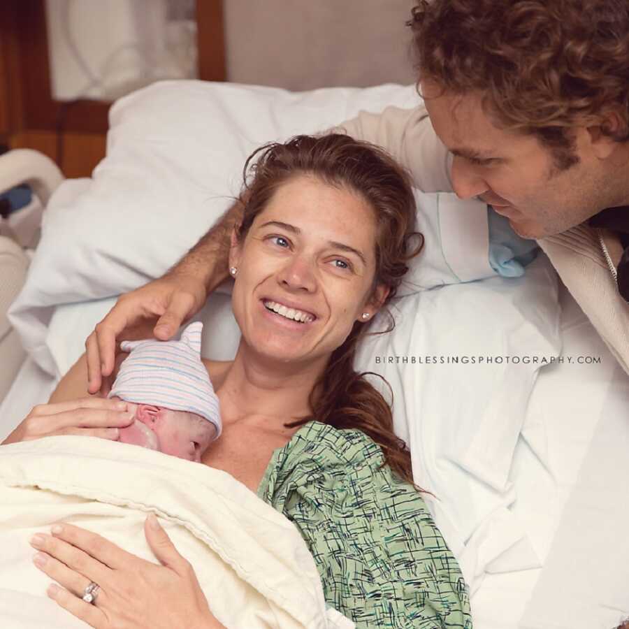 mother and father stare at each other while holding newborn baby girl right after childbirth 