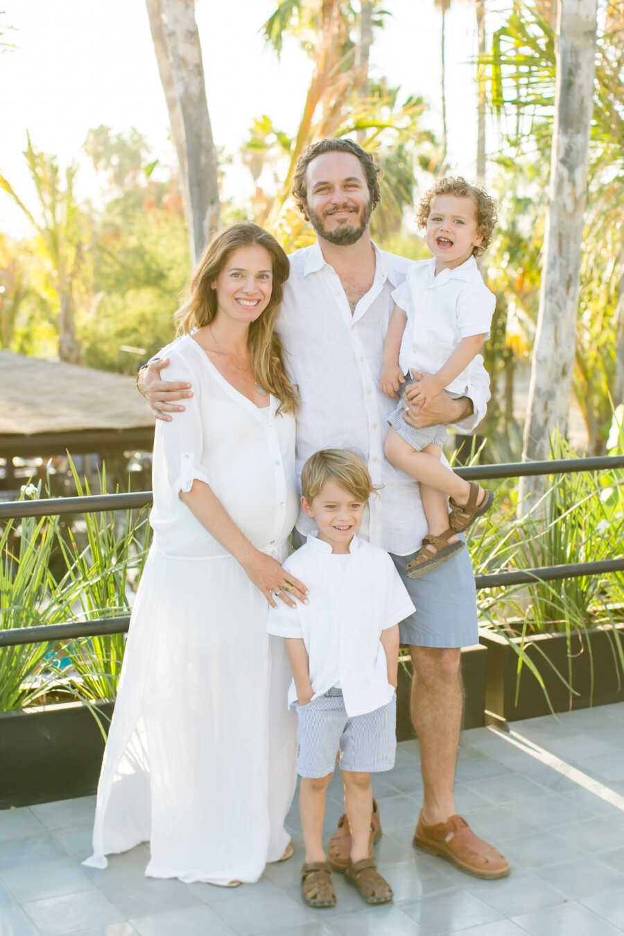 outdoors family portrait of mom dad and two sons wearing white matching outfits 