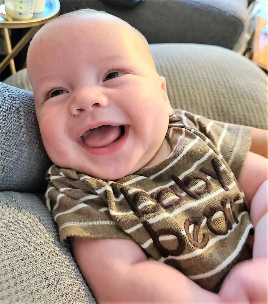 Mom takes a photo of her baby smiling big while wearing a 'baby bear' onesie