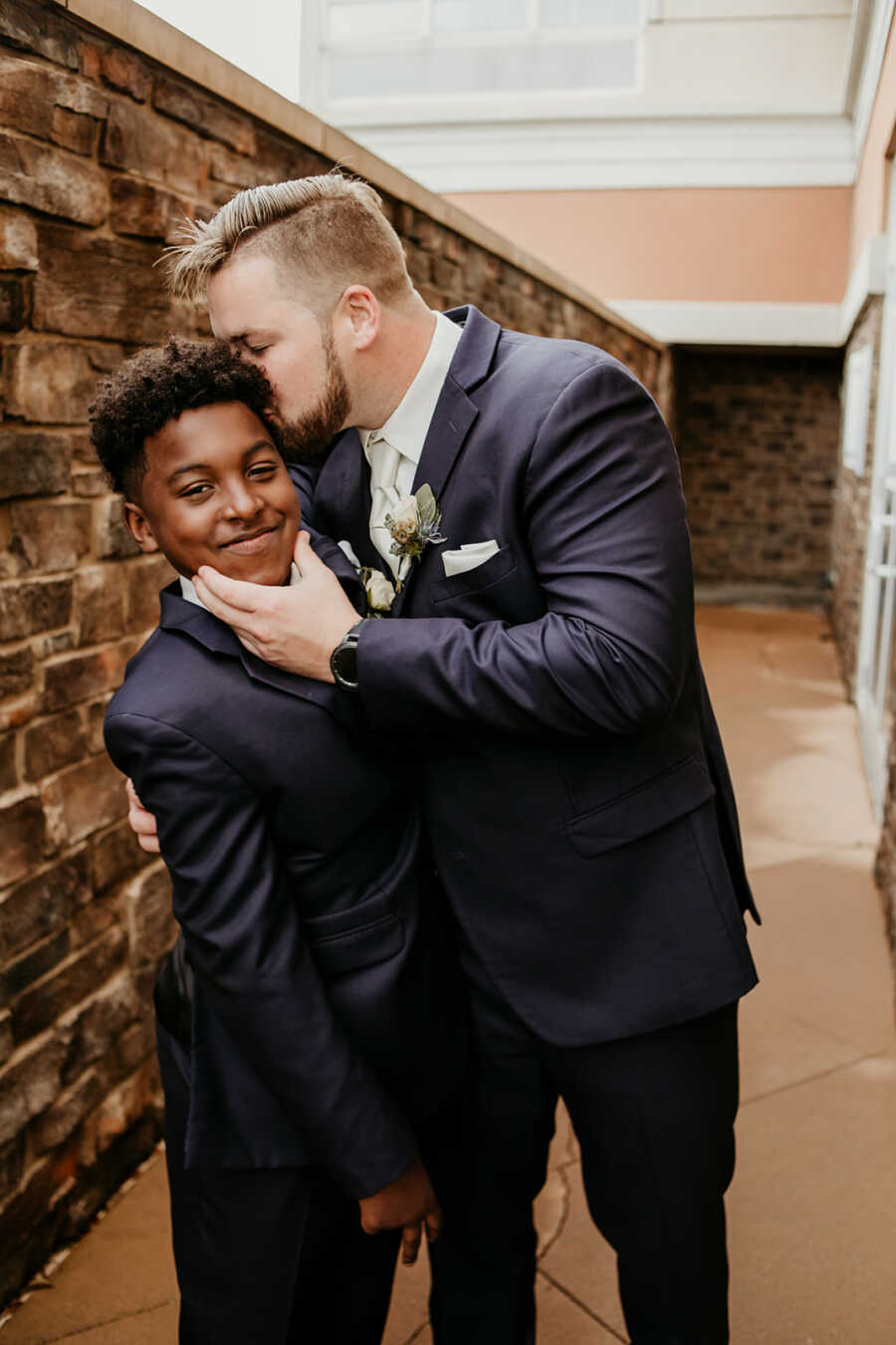 Stepdad kisses his stepson's forehead during wedding photos