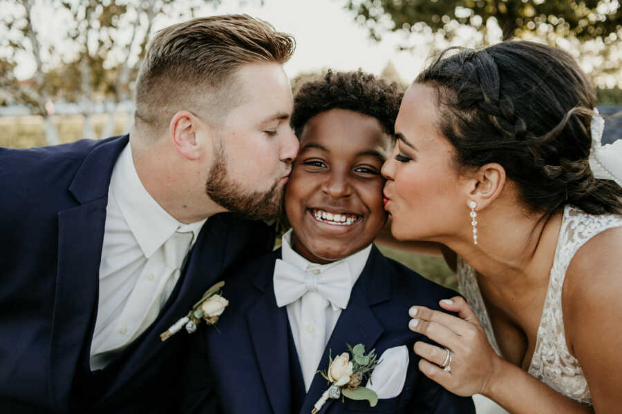 Mom and stepdad kiss their son on the cheek during wedding photos