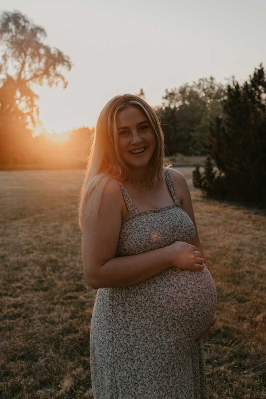 mom holding her baby belly smiling in the sunset
