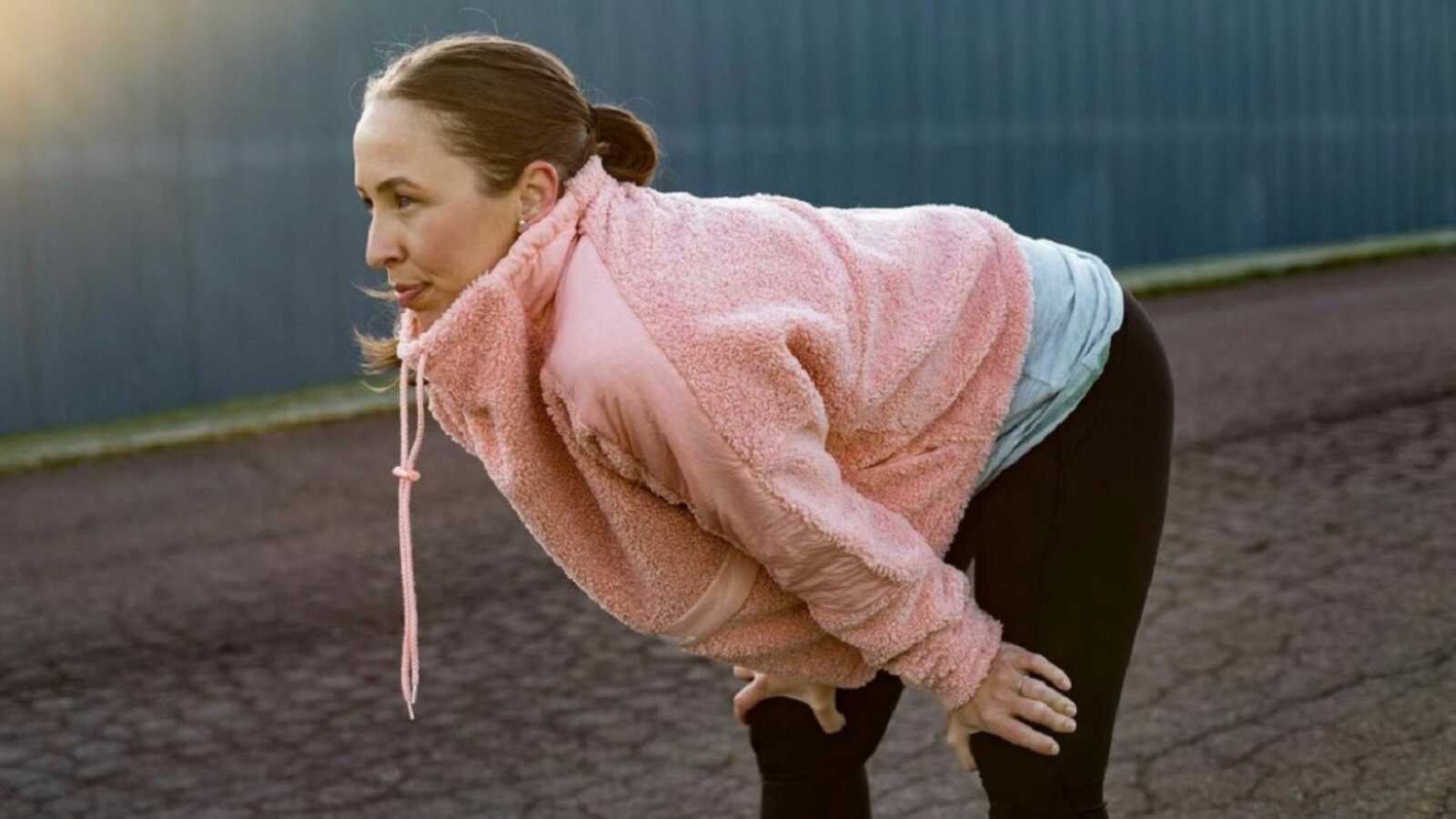 Mom leans over and rests during a workout in a pink hoodie
