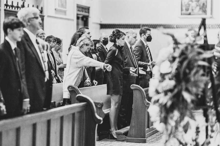 widow holds hands of friends and family during husband's funeral at catholic church