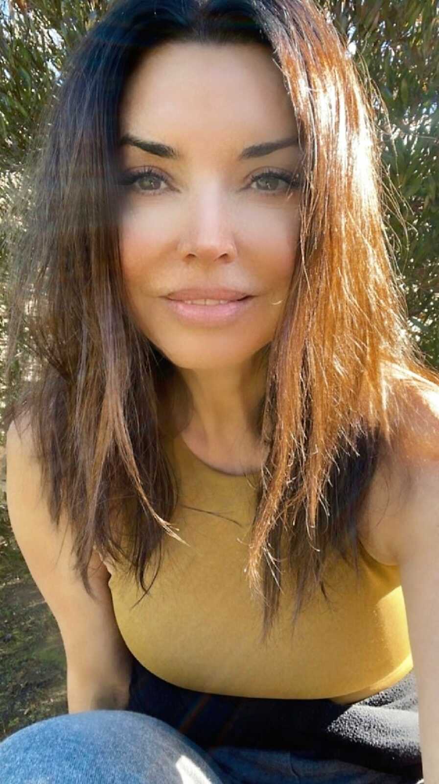 Empowerment coach for adult adoptees taking a selfie with the sunlight of the left side of her face and wearing a mustard yellow top