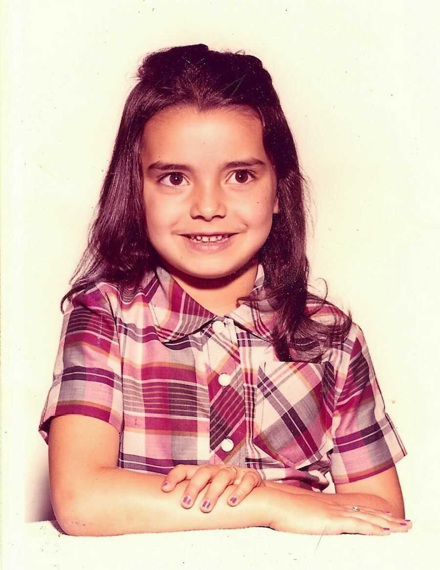 international adoptee wearing a plaid shirt with her arms crossed on a table 