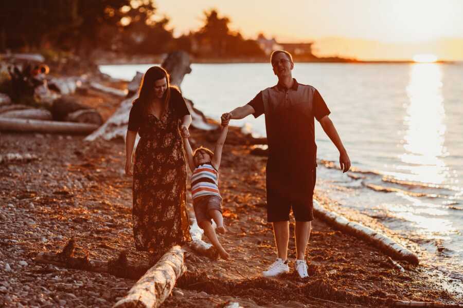 Couple swing their son while enjoying family time at the beach