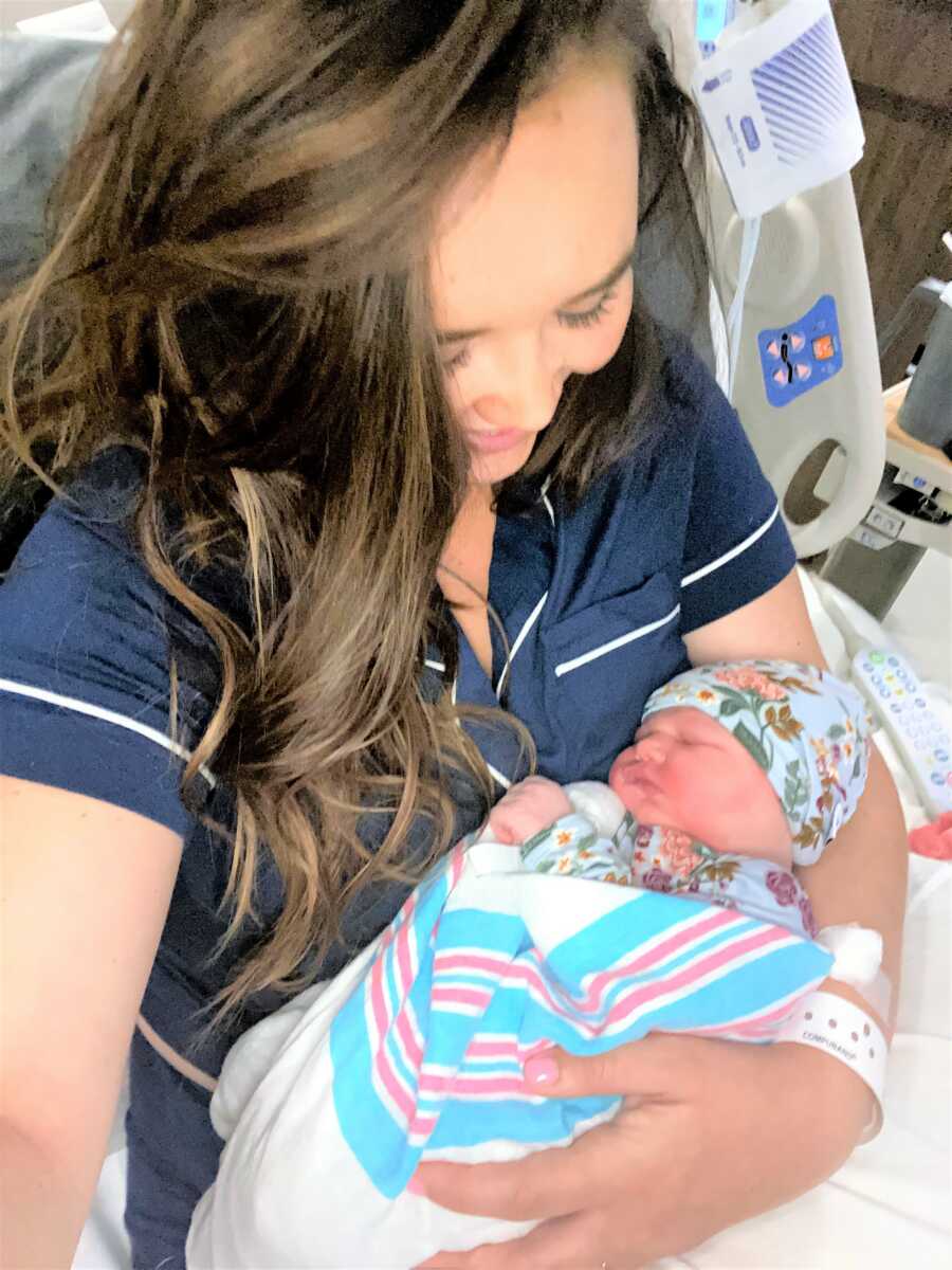 New mom holding her newborn baby wearing a blue onesie with floral print 