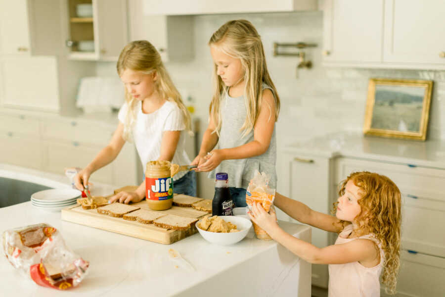 Three young girls help their mom make PB&Js during lunchtime