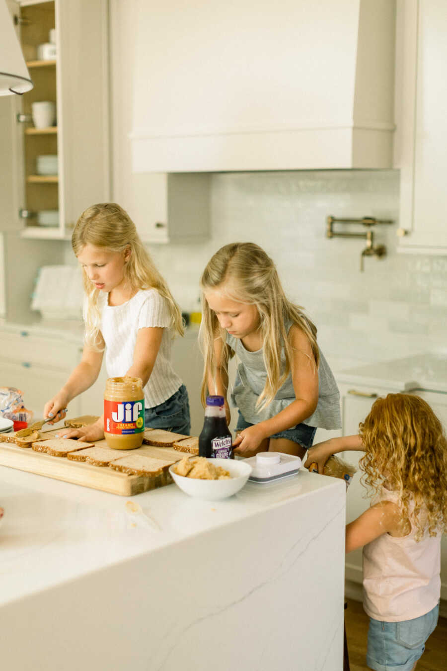 Little girls help their mom with lunch by assembling sandwiches