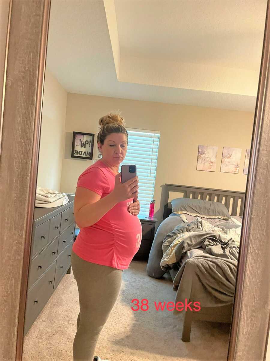 woman showing 38 week pregnant belly on a mirror selfie in her room 