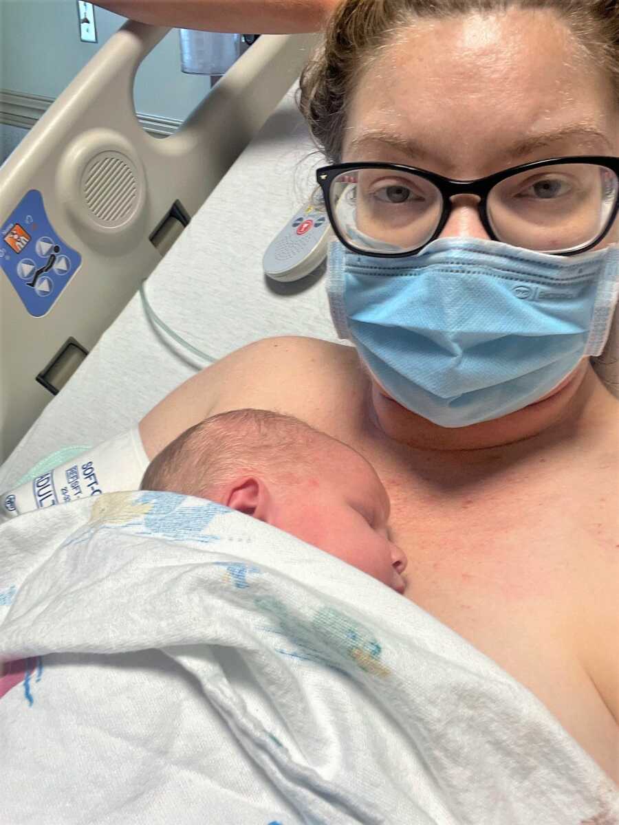 New mom battling COVID holding her newborn baby girl after childbirth wearing a mask 